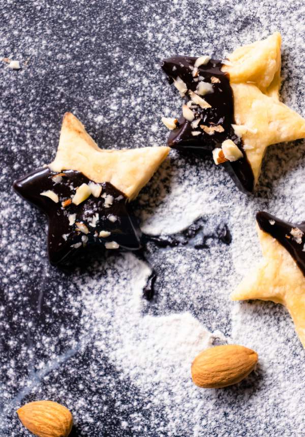 Holiday Shortbread Star Shaped Cookies on a black surface with sugar powder and almonds beside