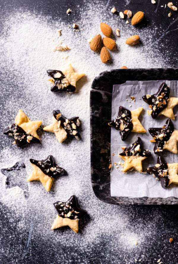 Holiday Shortbread Star Shaped Cookies some kept on a black plate while some arranged on the black table with some almonds around