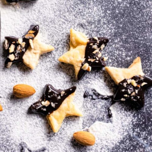 Holiday Shortbread Star Shaped Cookies arranged on a black table with powdered sugar and almonds beside