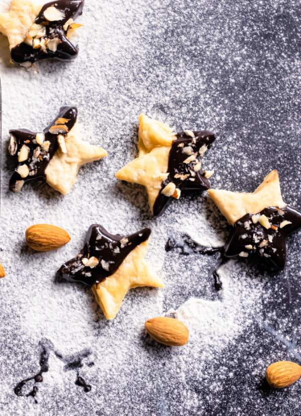 Holiday Shortbread Star Shaped Cookies arranged on a black table with powdered sugar and almonds beside