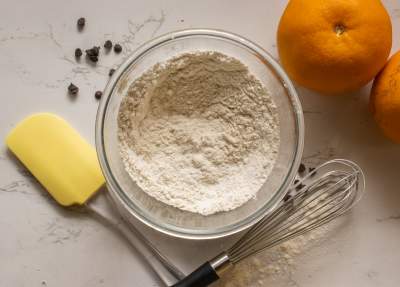 Dry ingredients in a bowl with spatula and oranges beside